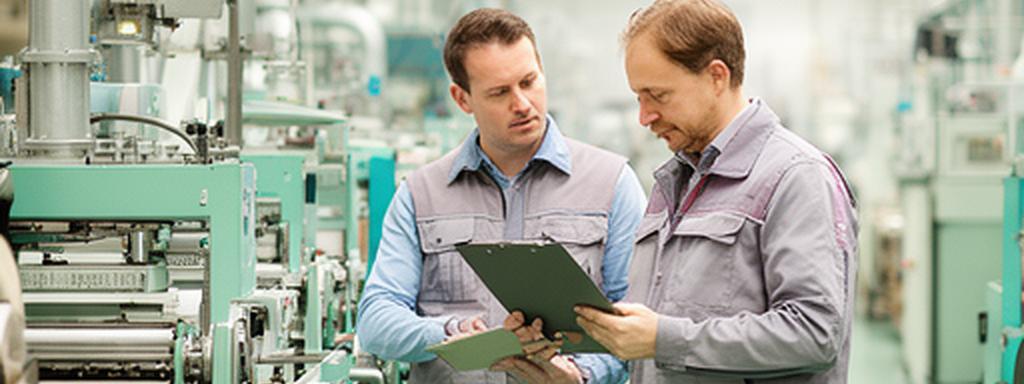 Resource optimisation adviser reviewing factory production figures with a plant supervisor beside organised equipment